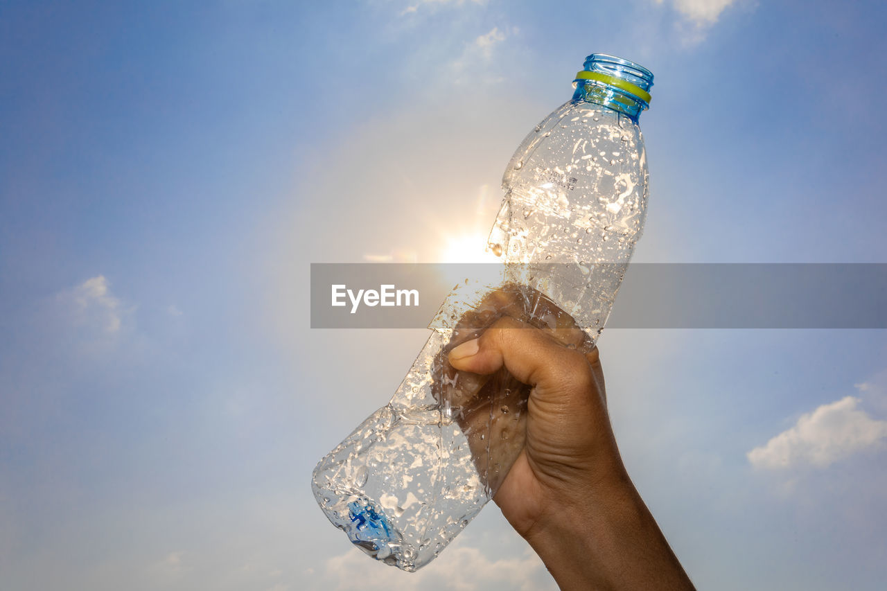 Person holding bottle against sky
