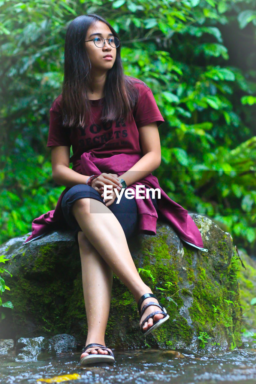 Young woman looking away while sitting on tree