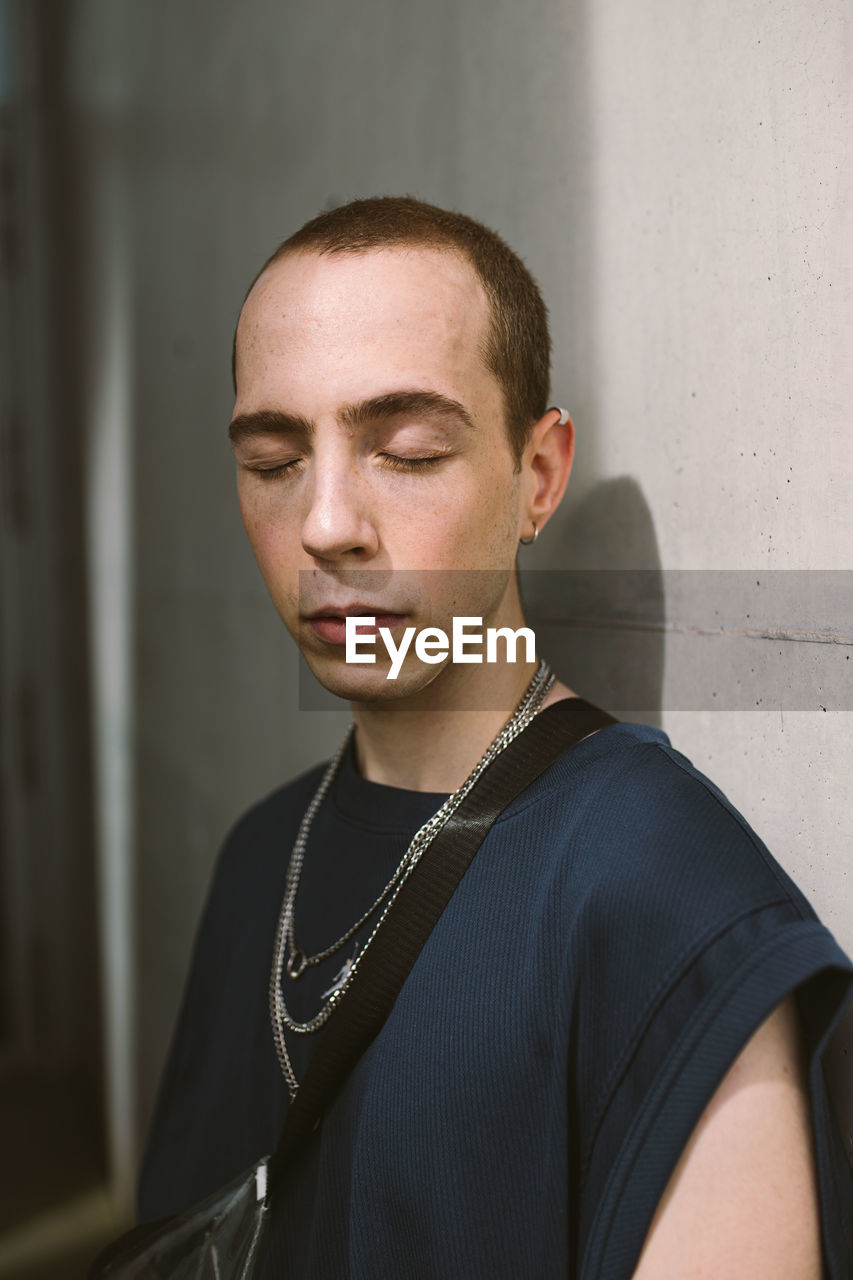 Young man with eyes closed standing against wall