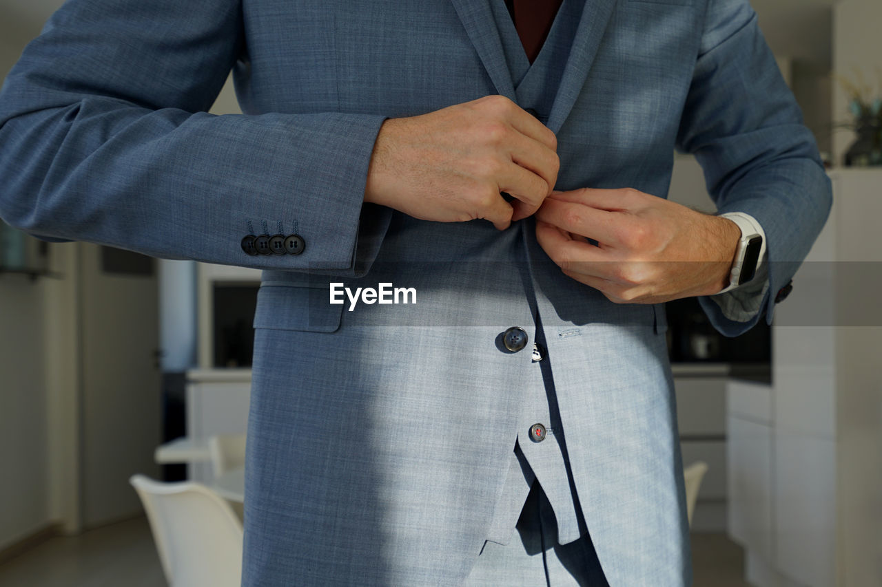 Midsection of businessman buttoning blazer at home