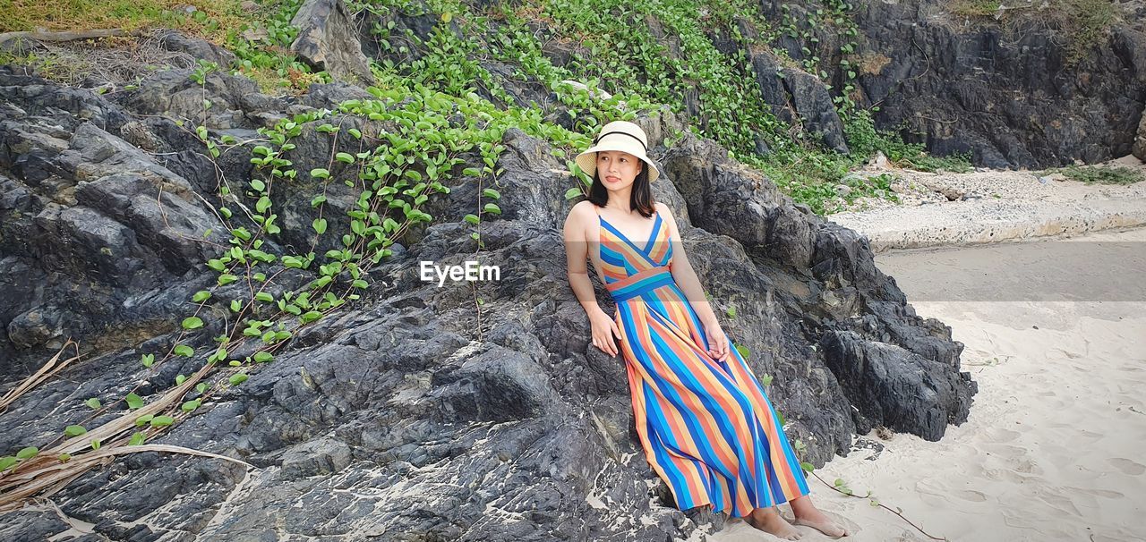 Young woman looking away while standing by rock at beach