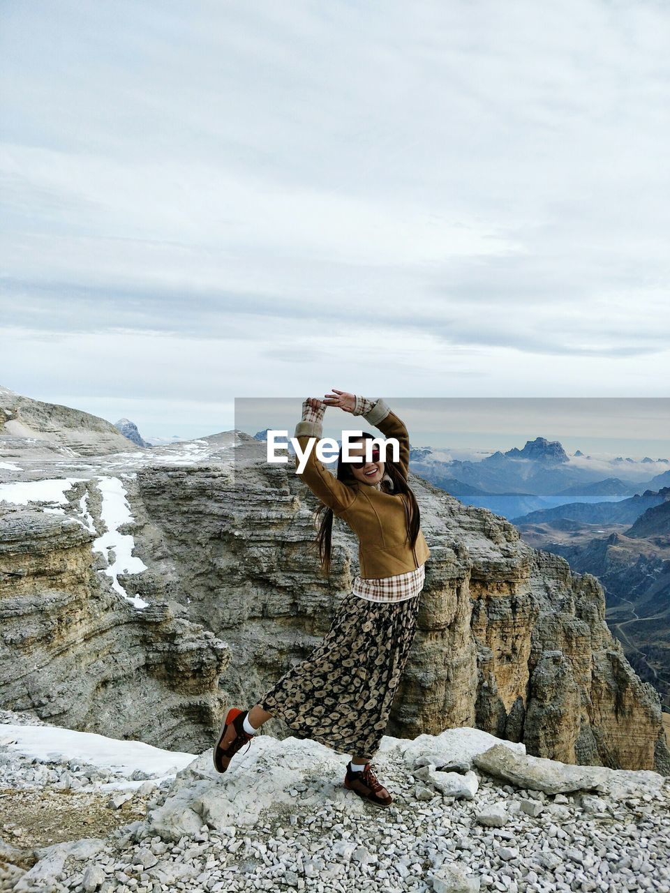 Portrait of woman dancing on mountain against cloudy sky