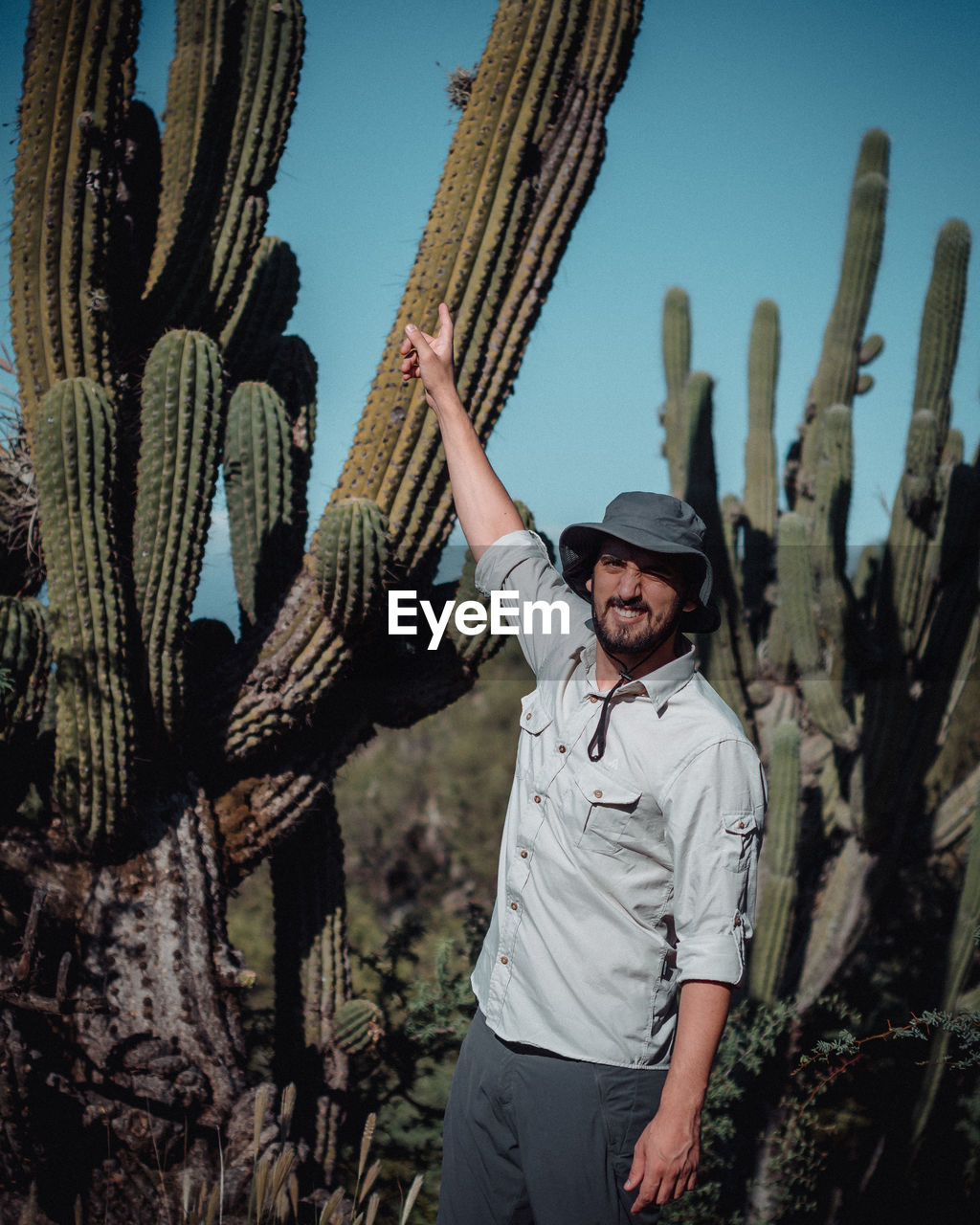 FULL LENGTH PORTRAIT OF YOUNG MAN STANDING BY CACTUS