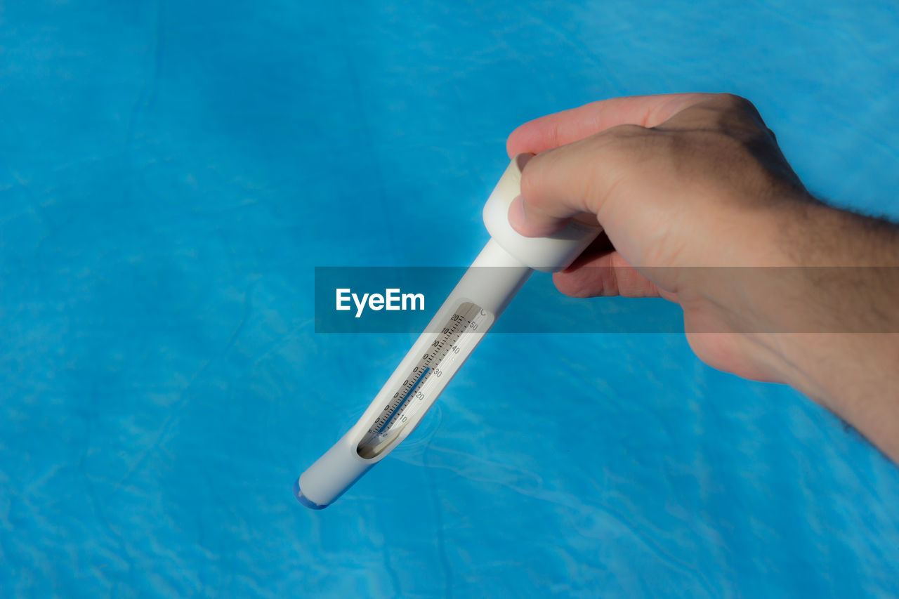 Cropped hand holding thermometer in swimming pool during sunny day