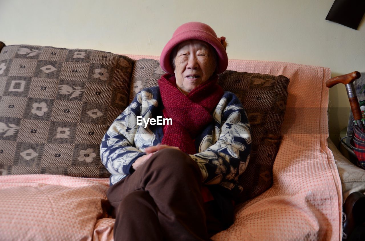 Senior woman wearing warm clothing sitting on sofa at home