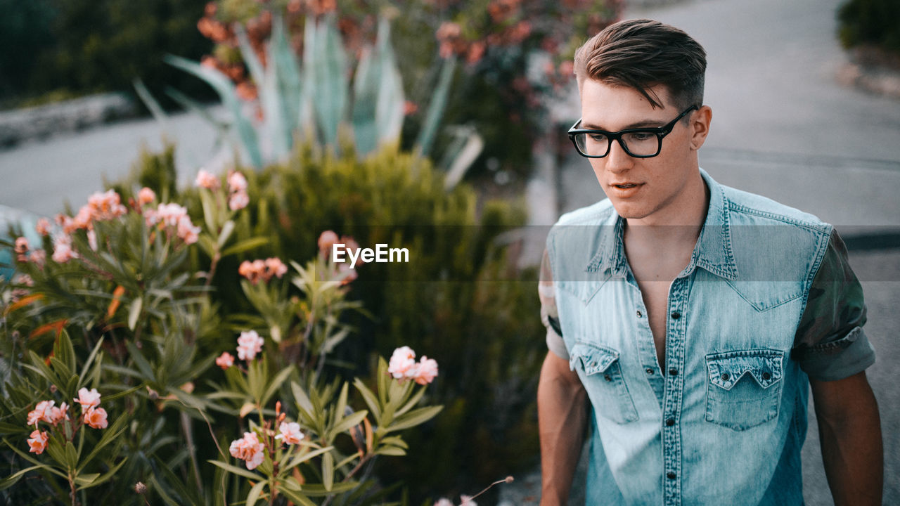 Young man wearing eyeglasses by flowers at park