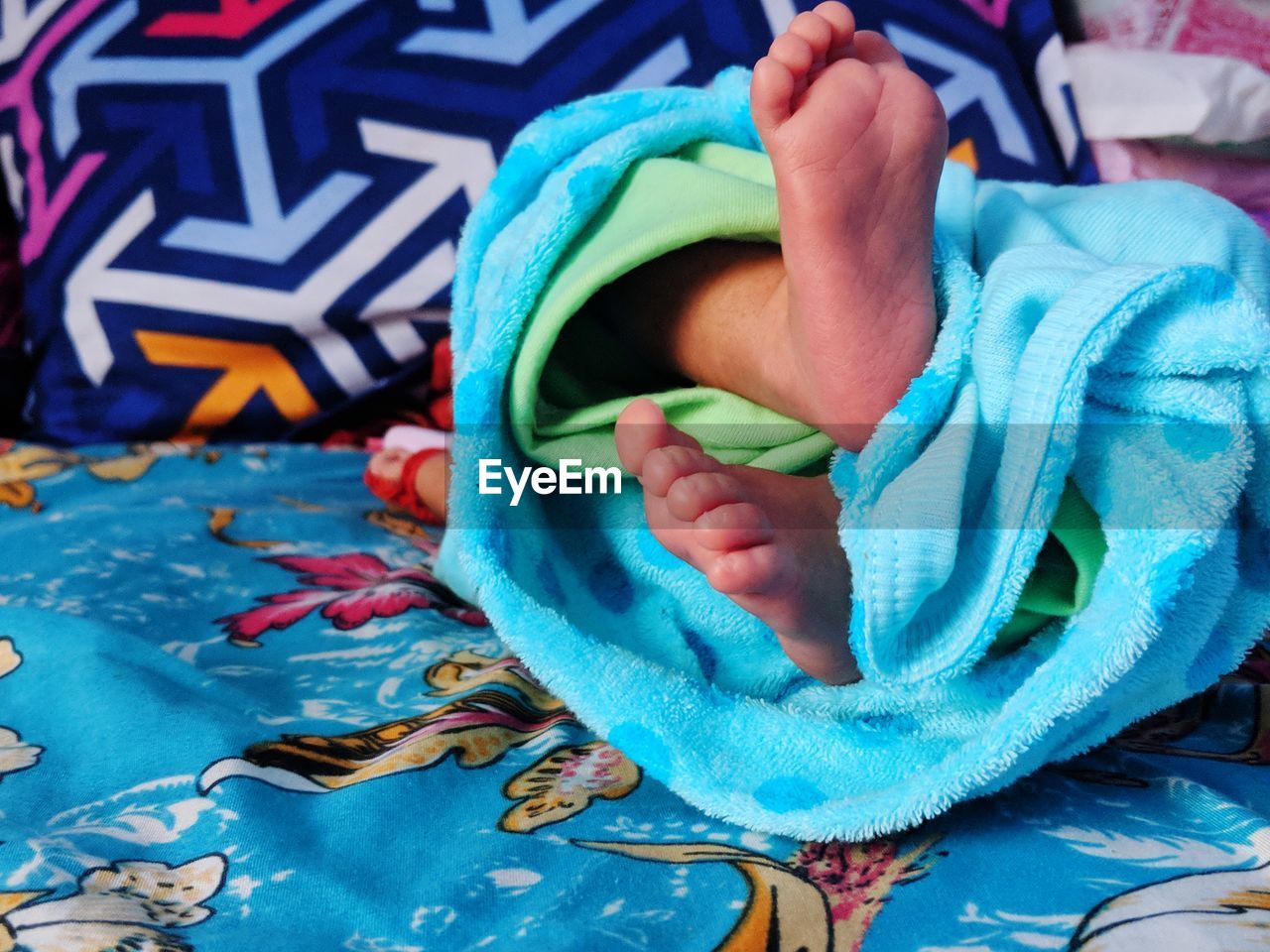Low section of baby wrapped in blanket lying on bed at home