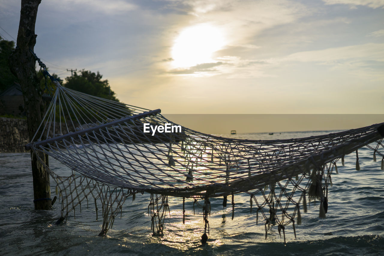 Empty hammock over sea against sky during sunset