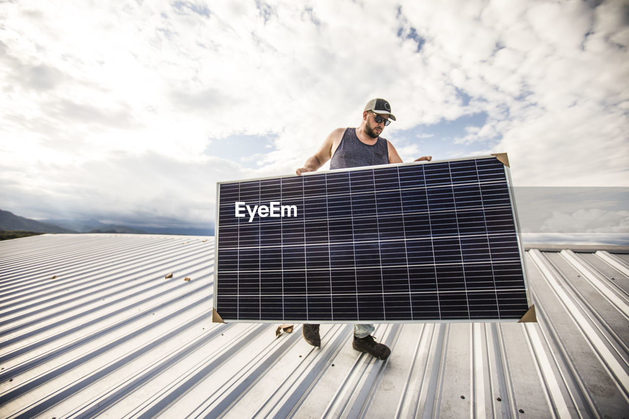 Man carrying solar panel on roof during installation.