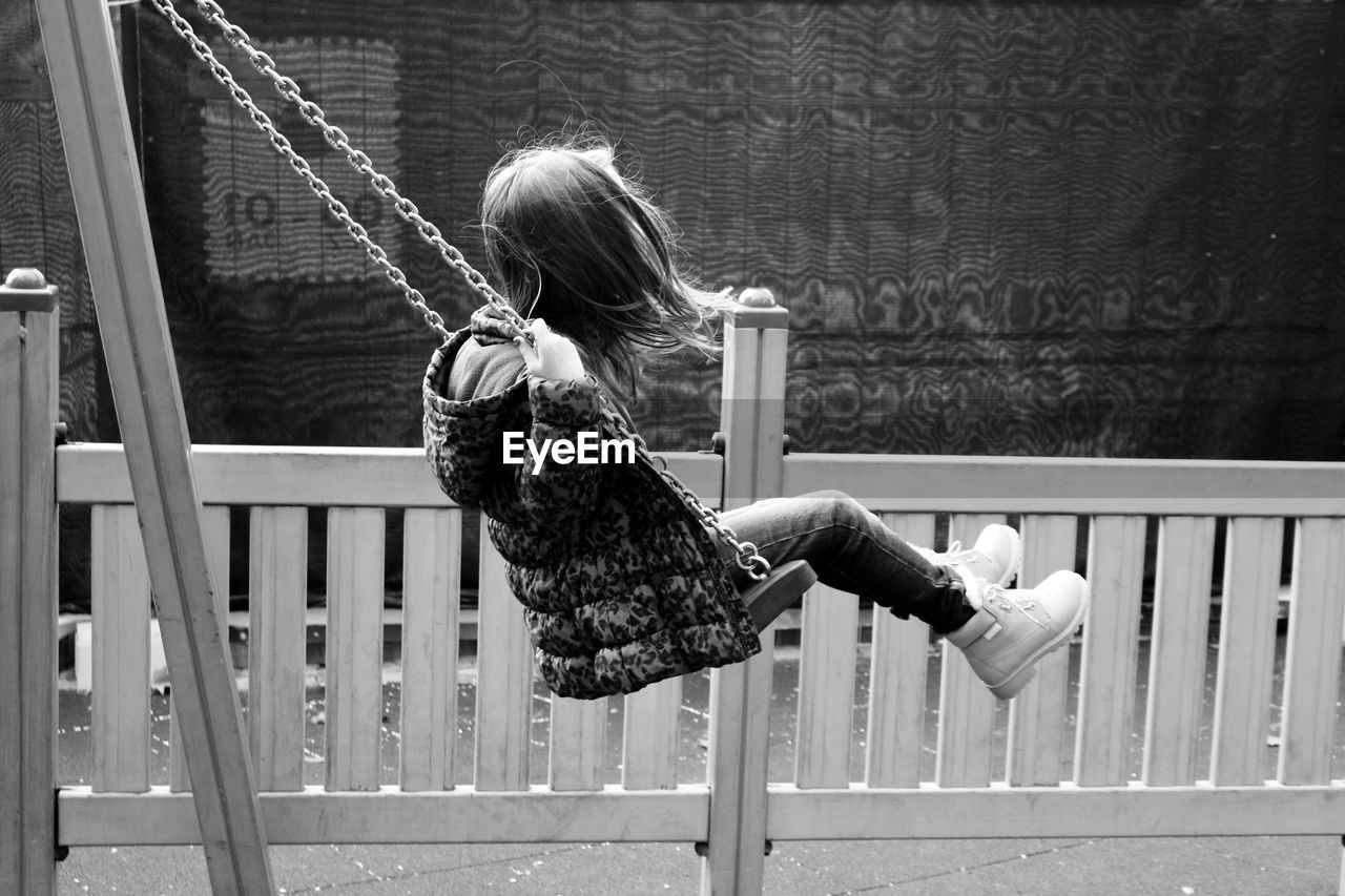 Side view of girl enjoying swing at playground