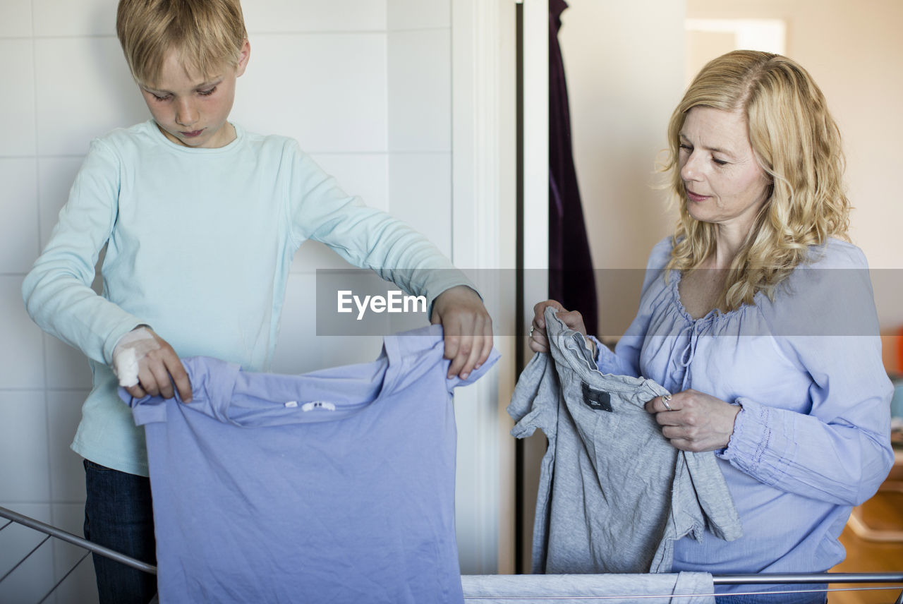 Mother and son drying laundry on rack at home
