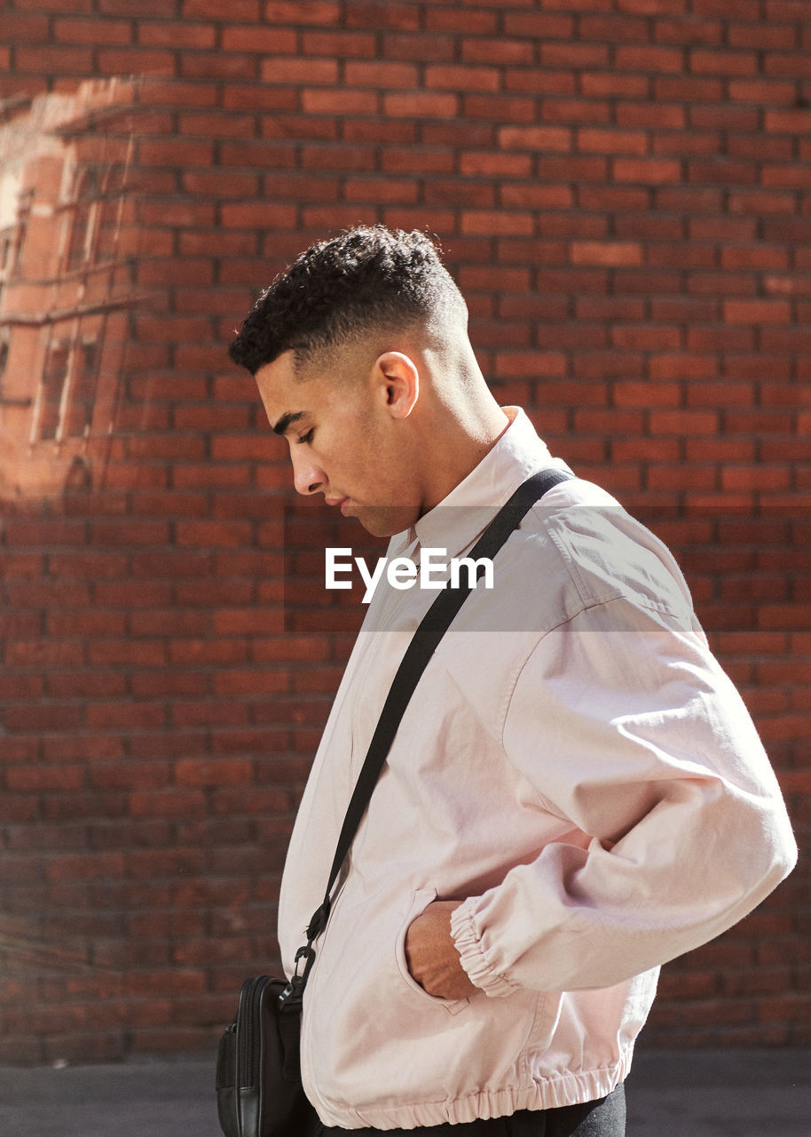 Side view of young man standing against brick wall