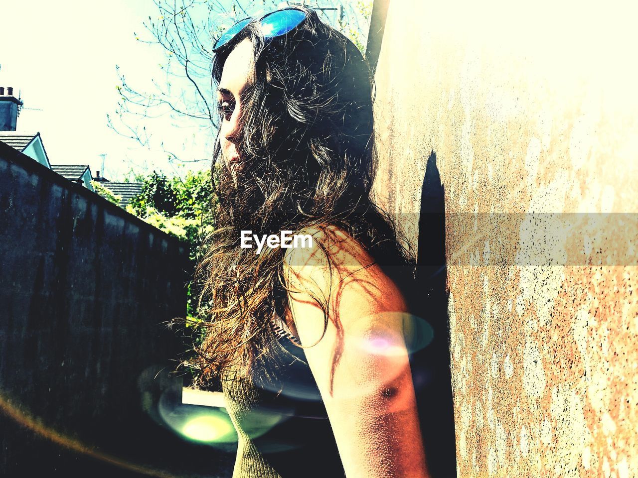 Low angle view of young woman standing by wall on sunny day