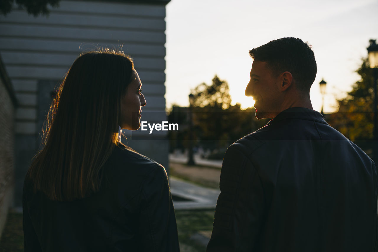 Couple looking at each other while standing outdoors during sunset