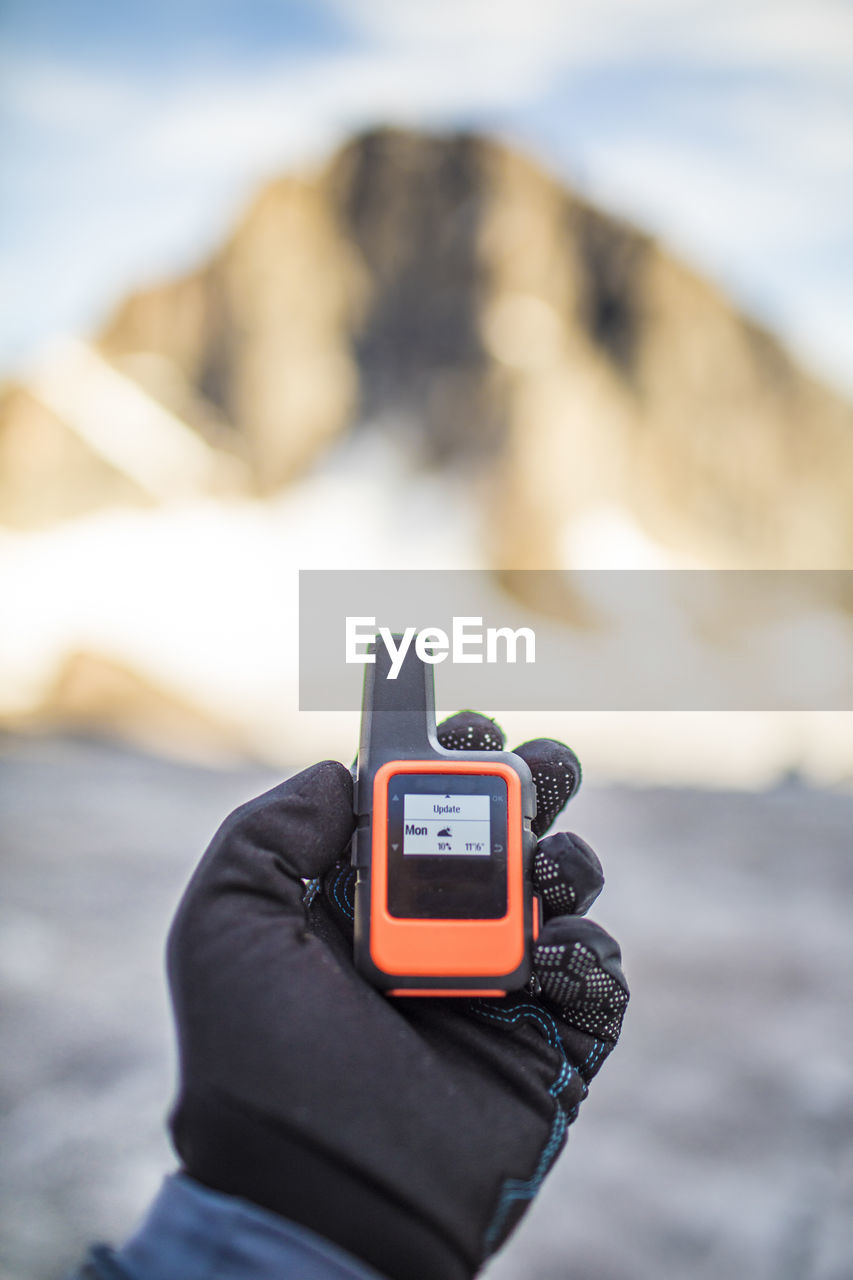 Mountaineer holding mini gps unit with weather forecast showing.