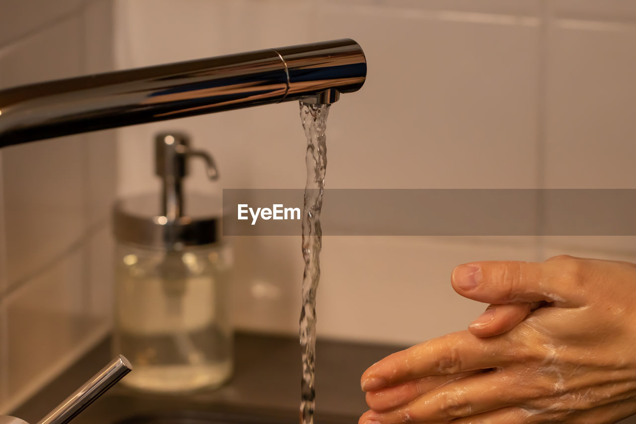 MIDSECTION OF PERSON HOLDING FAUCET AGAINST WHITE WALL