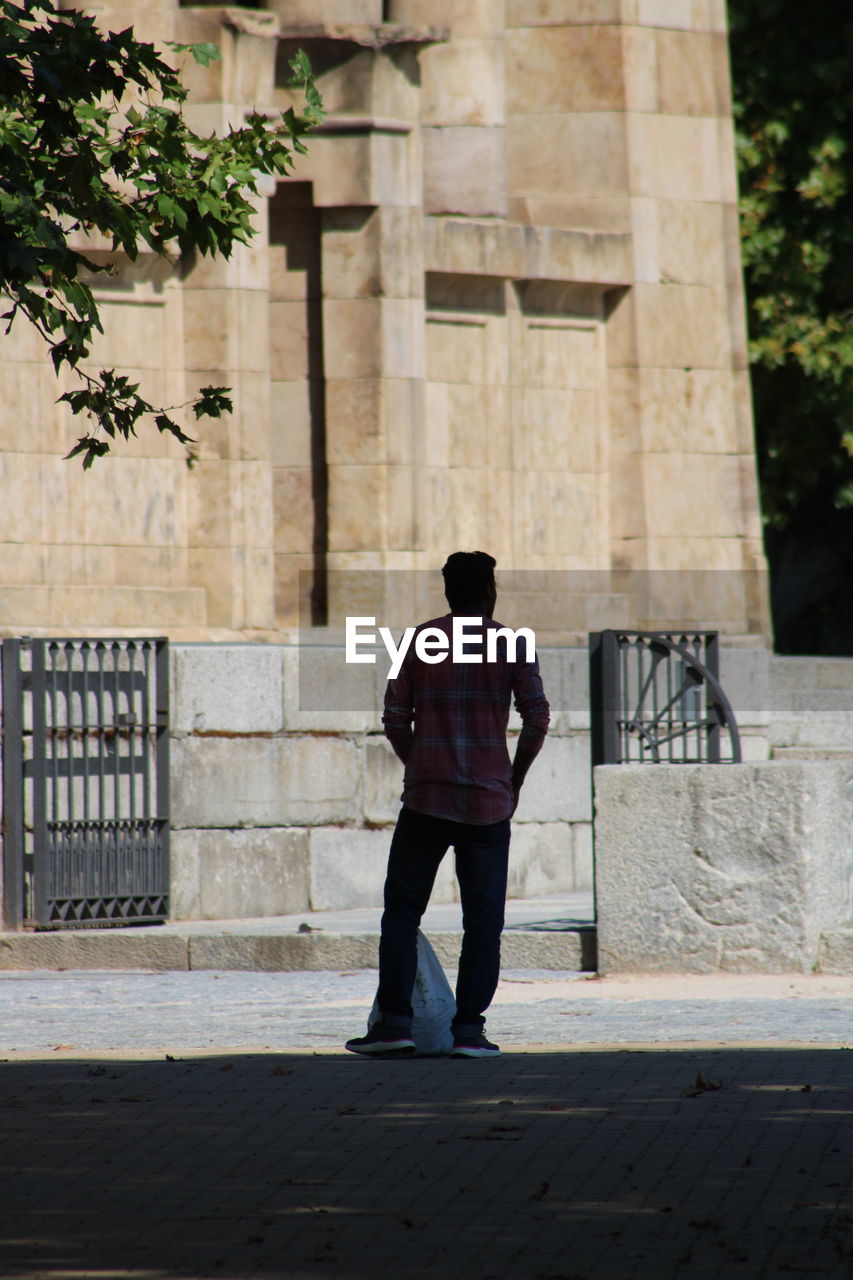 REAR VIEW OF MAN STANDING BY BUILDING AGAINST TREES