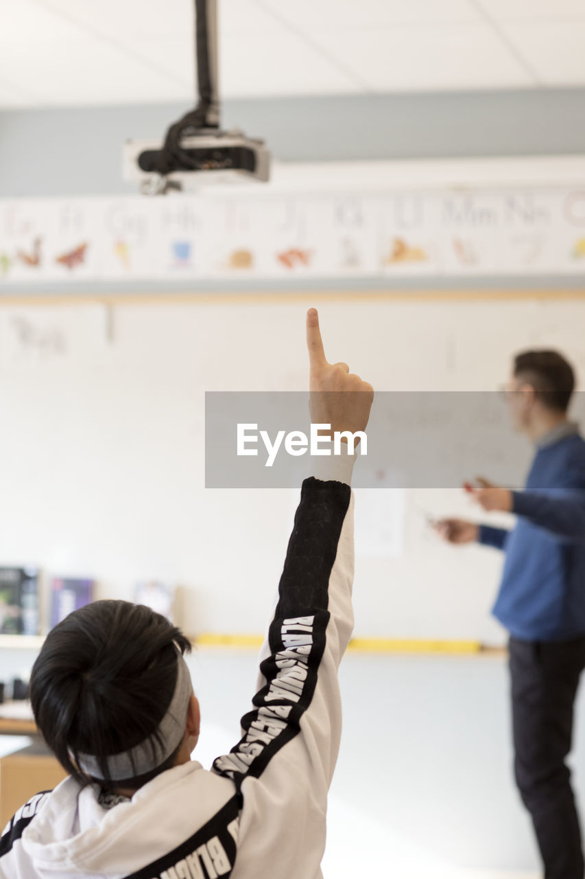 Teenage boy raising hand in classroom