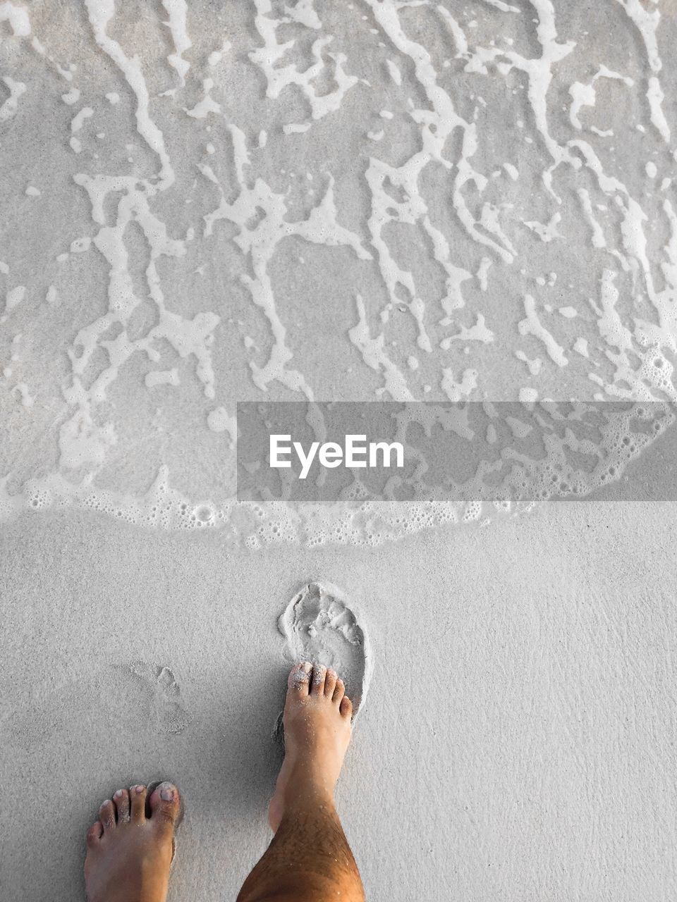 Low section of person standing on wet sand