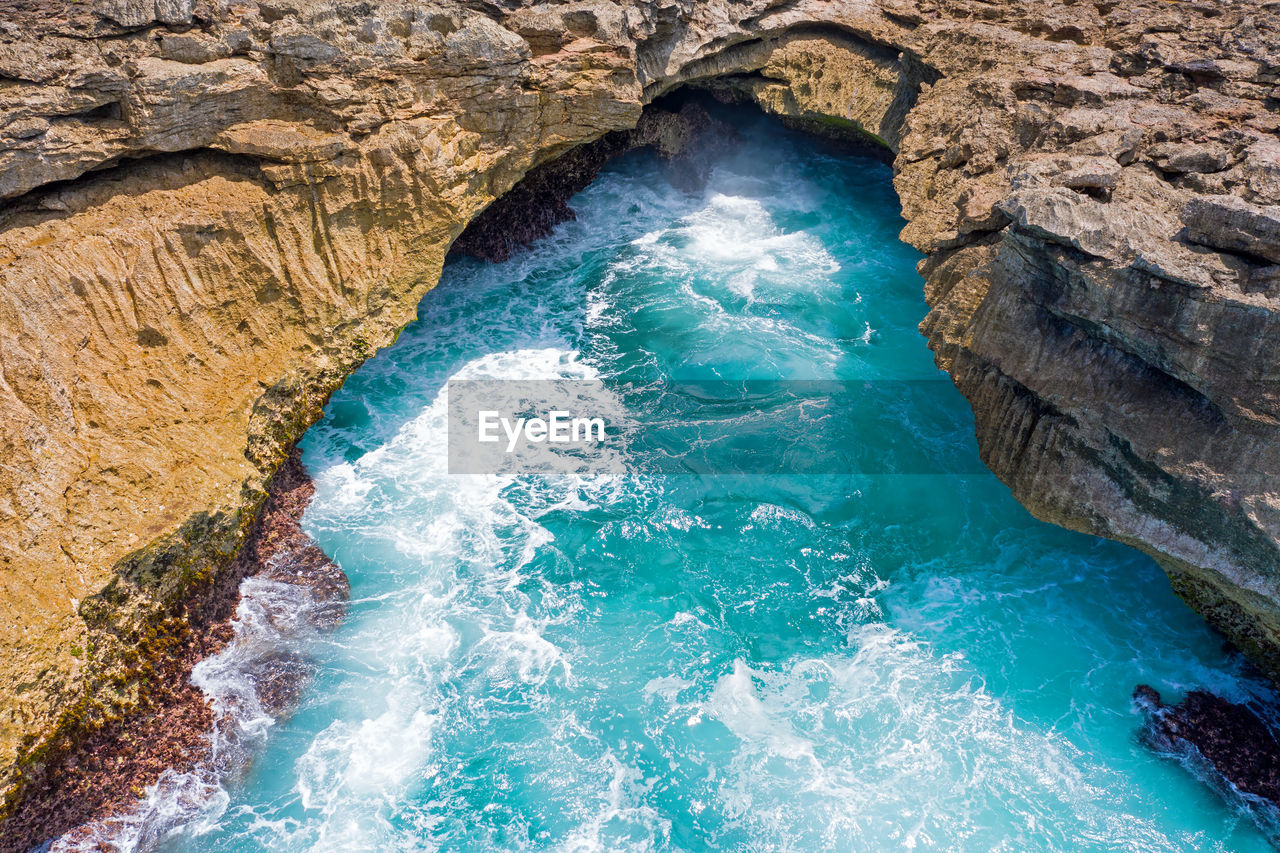 High angle view of waves splashing in sea by cliff