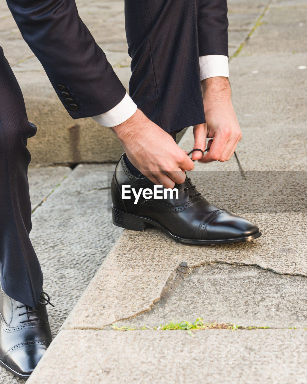 Low section of man standing on street lacing his shoes