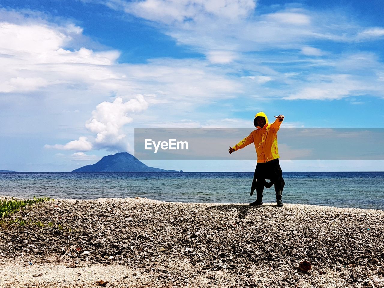 Man gesturing while standing at beach against cloudy sky