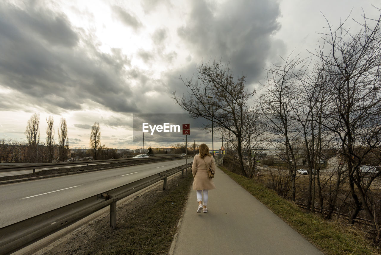 REAR VIEW OF WOMAN WALKING ON ROAD AMIDST BARE TREES