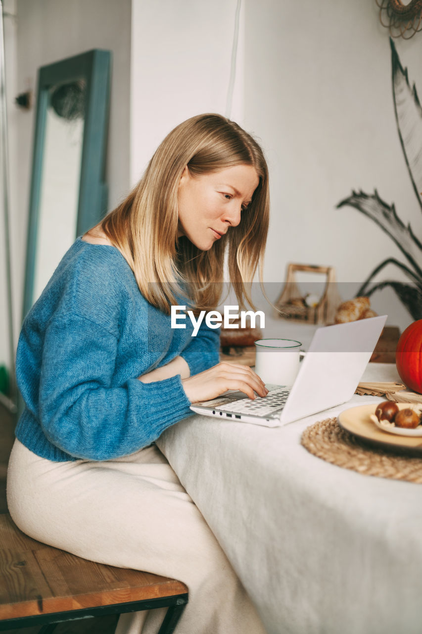 Cute blonde girl working in the morning on a laptop and drinking coffee. work online, freelance