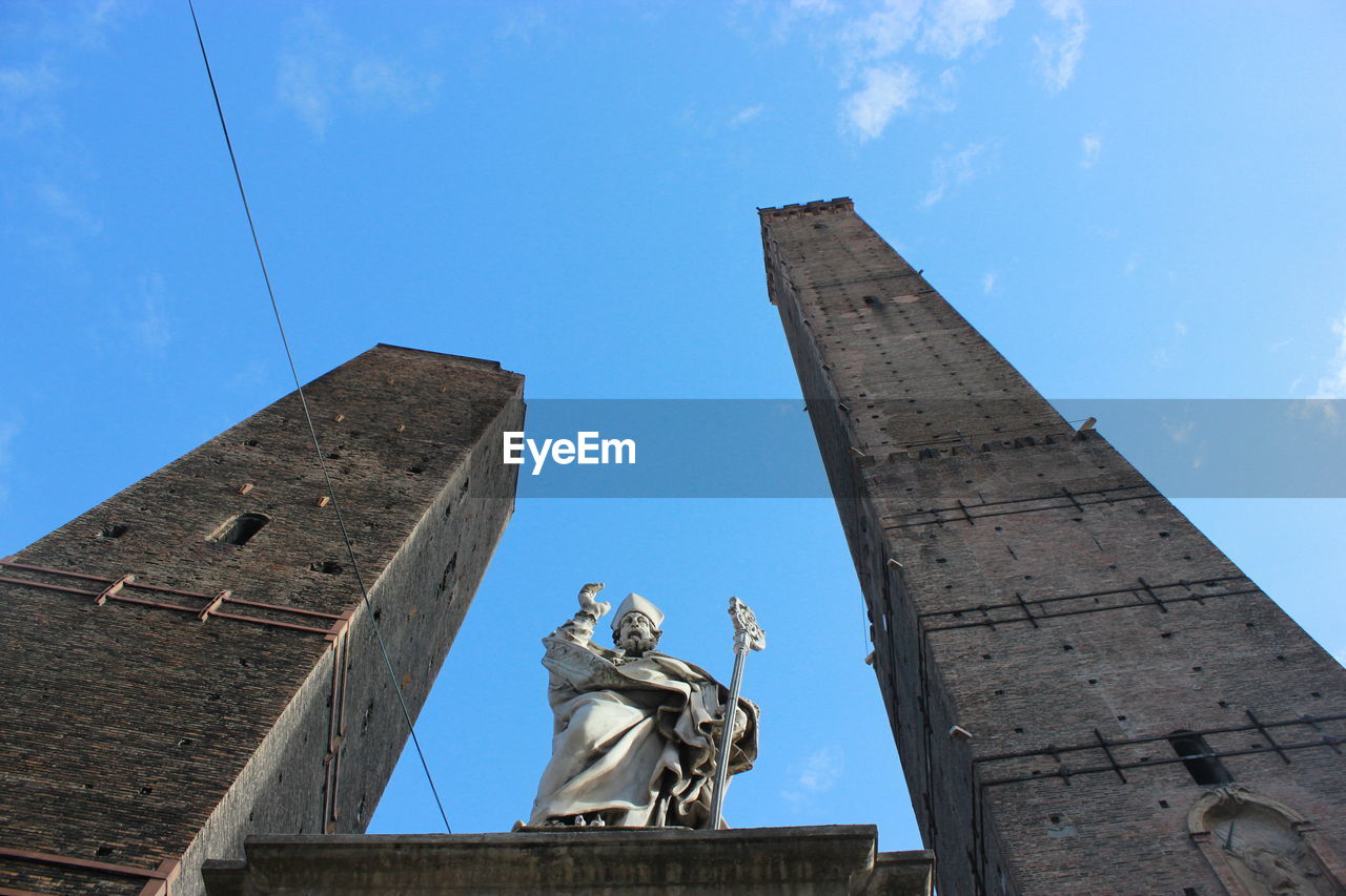 Low angle view of statue amidst towers against blue sky