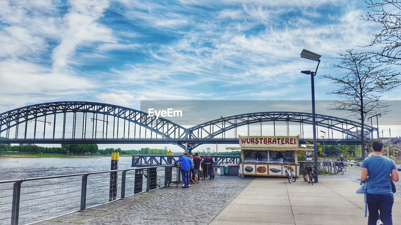 REAR VIEW OF MAN AND WOMAN ON BRIDGE AGAINST SKY