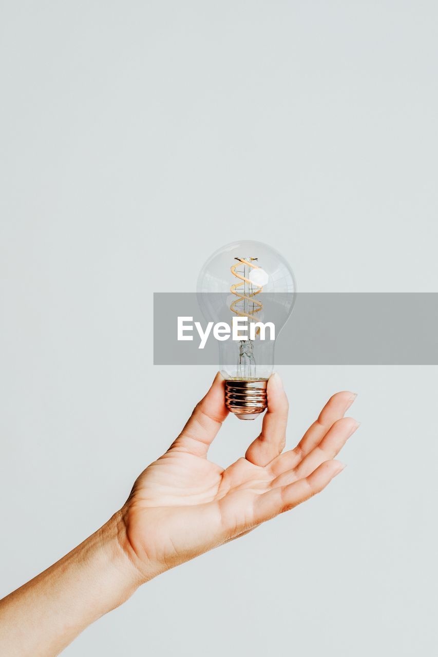 cropped hand of woman holding light bulb against white background