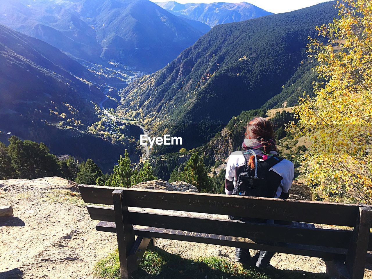 Rear view of woman sitting on bench against mountains