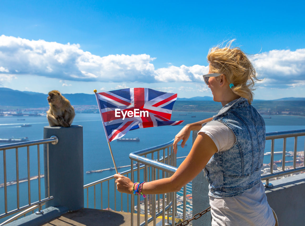 Woman with british flag standing by monkey at observation point against blue sky