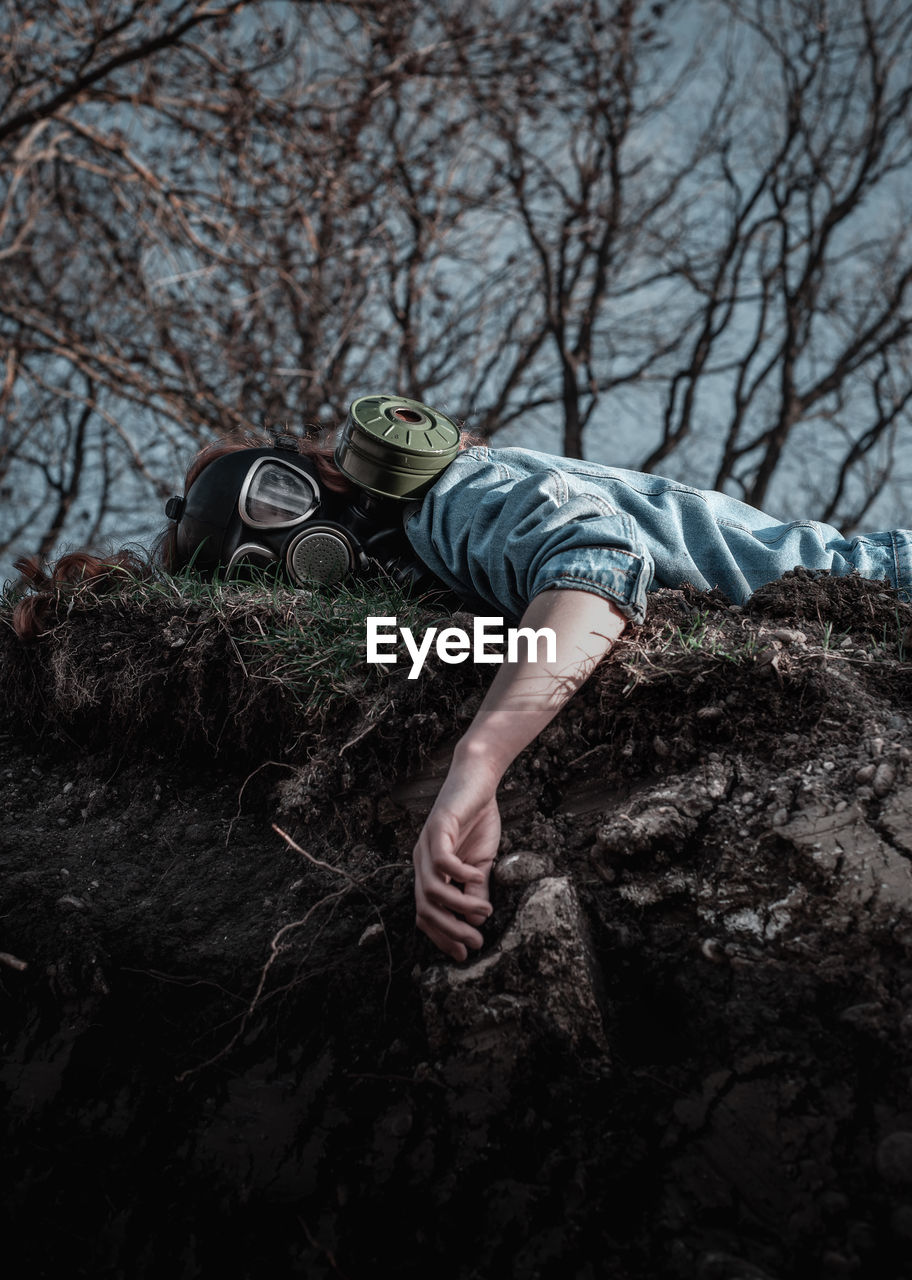 Low angle portrait of woman wearing gas mask while lying on land