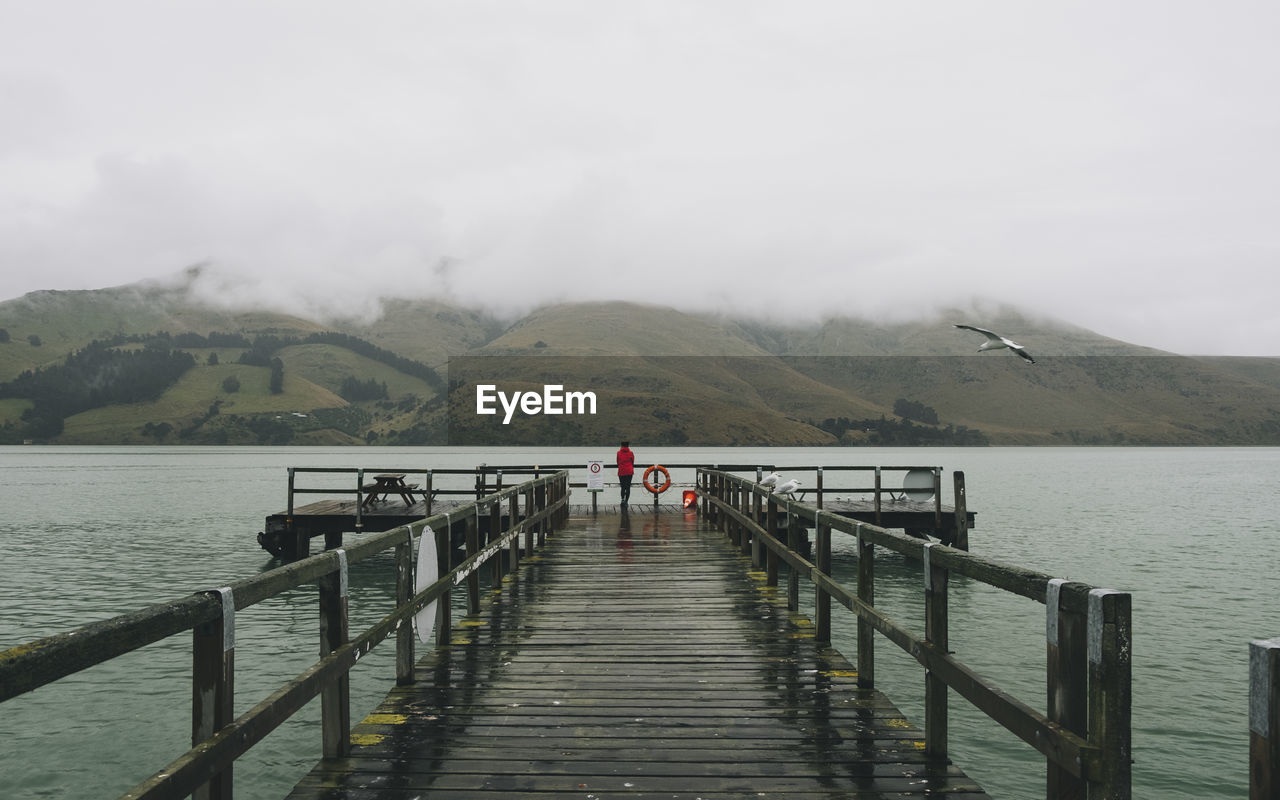 Woman on a red jacket standing at port levy jetty, banks peninsula, nz