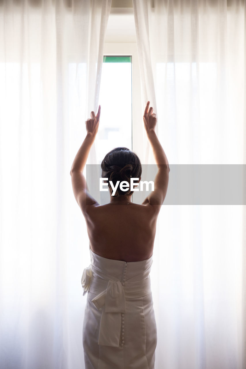 Rear view of bride opening curtain