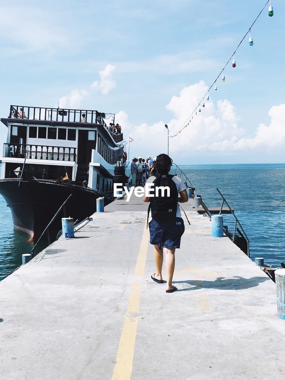 Rear view of man walking towards people by ferry moored in sea