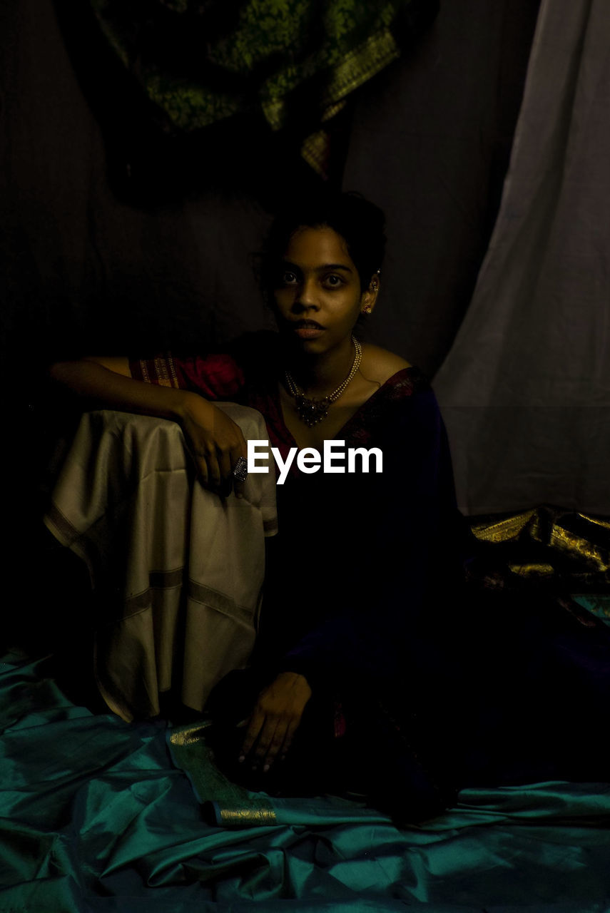 Portrait of young woman sitting on bed at home