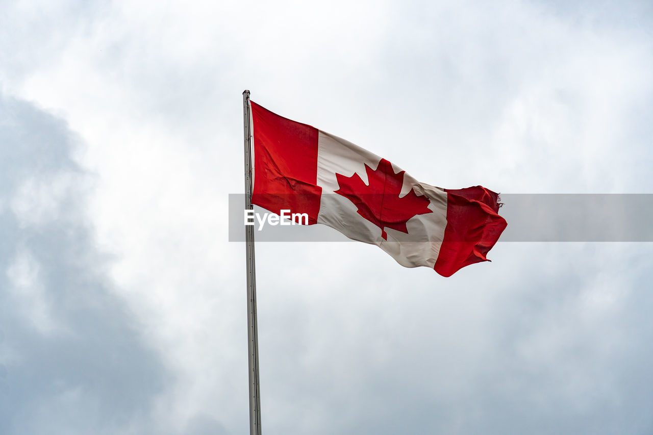 Low angle view of canadian flag waving on pole against sky