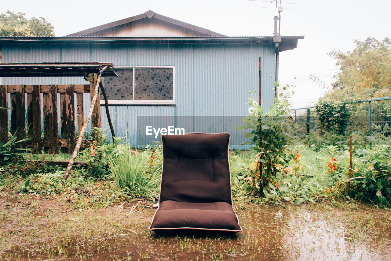 Empty seat in wet yard by house against clear sky