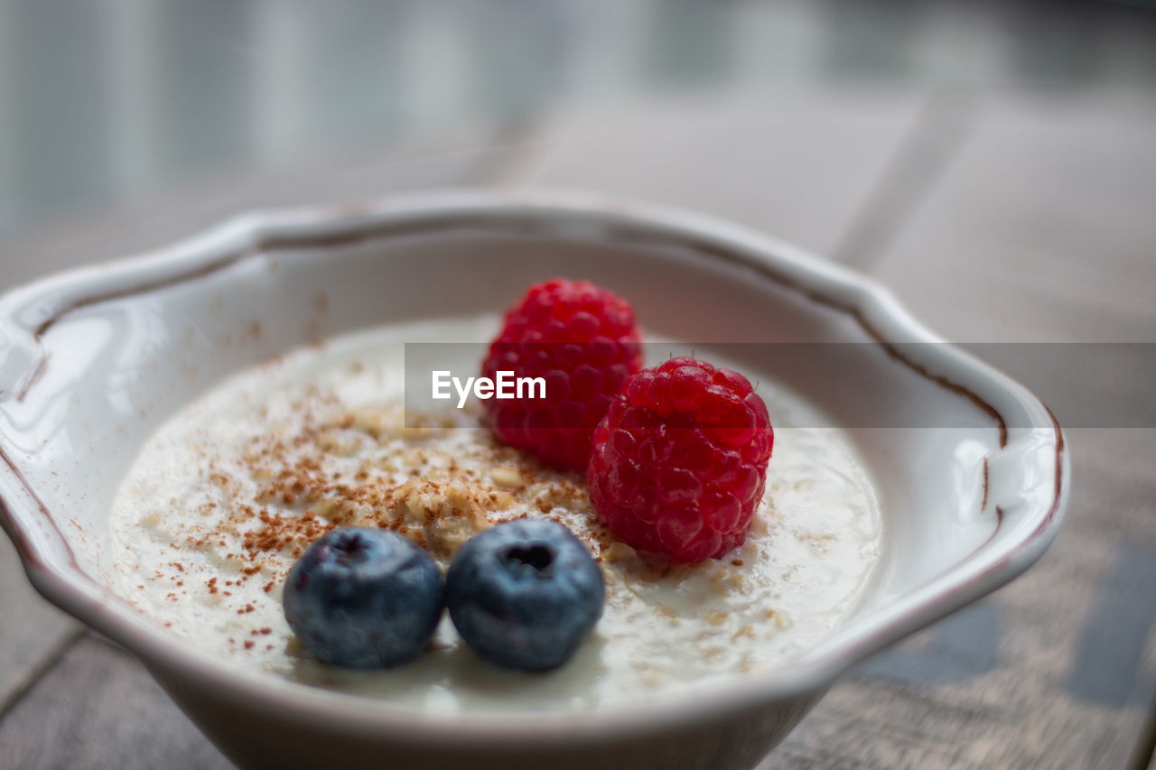 Close-up of porridge in a bowl with blueberries and raspberries on a wooden board