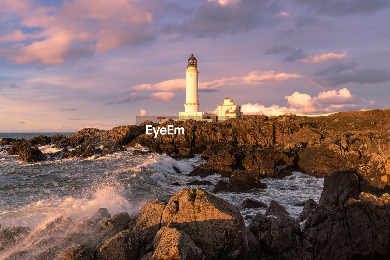 Lighthouse on rocks by sea against sky