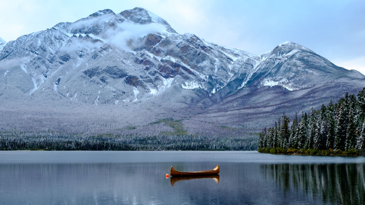 A lonesome canoe floats on a freezing water lake with surrounding snow covered mountains. 