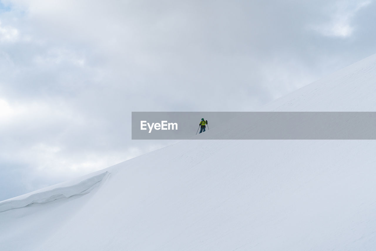 Low angle view of man standing on snowcapped mountain against sky