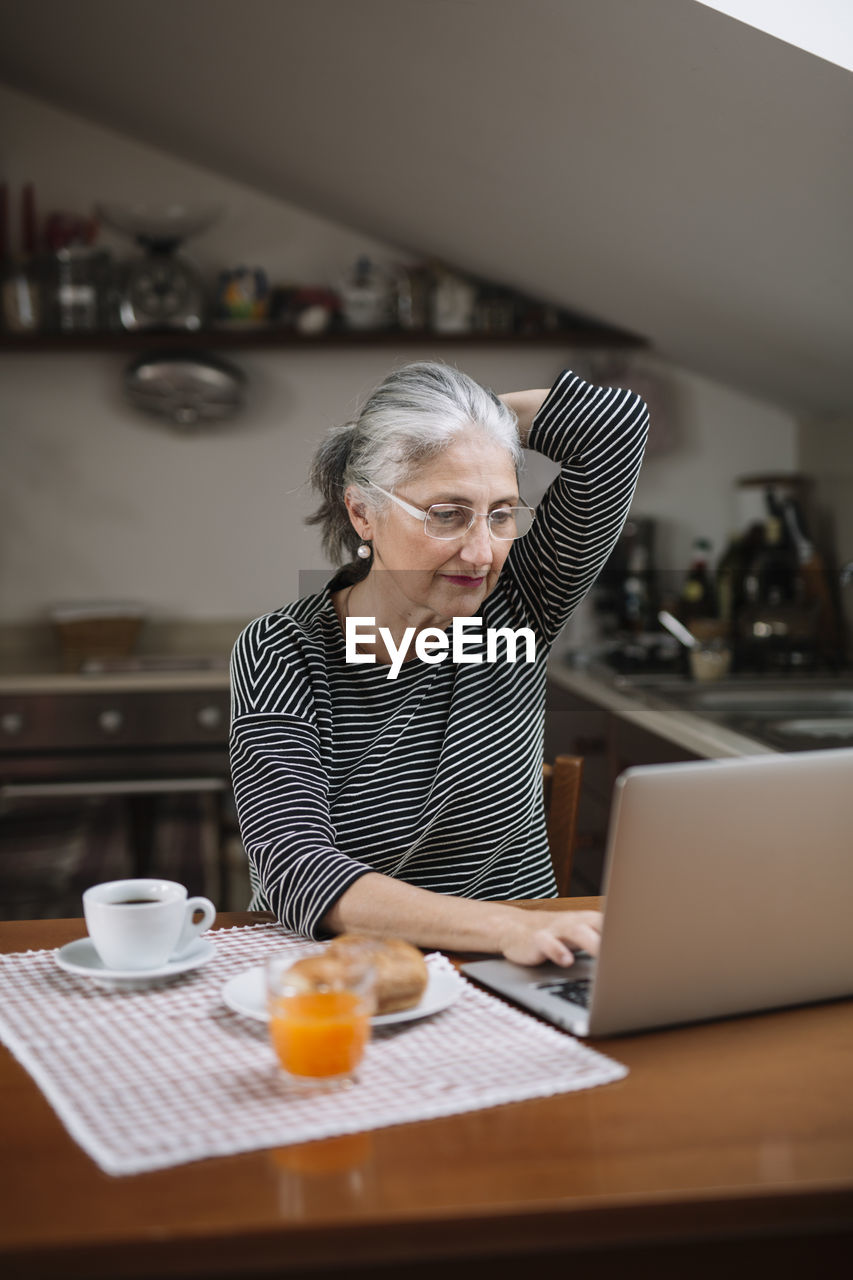 Portrait of senior woman using laptop at breakfast table