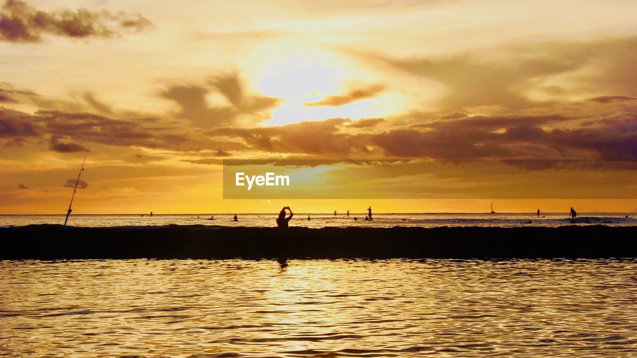 Silhouette people on sea against sky during sunset