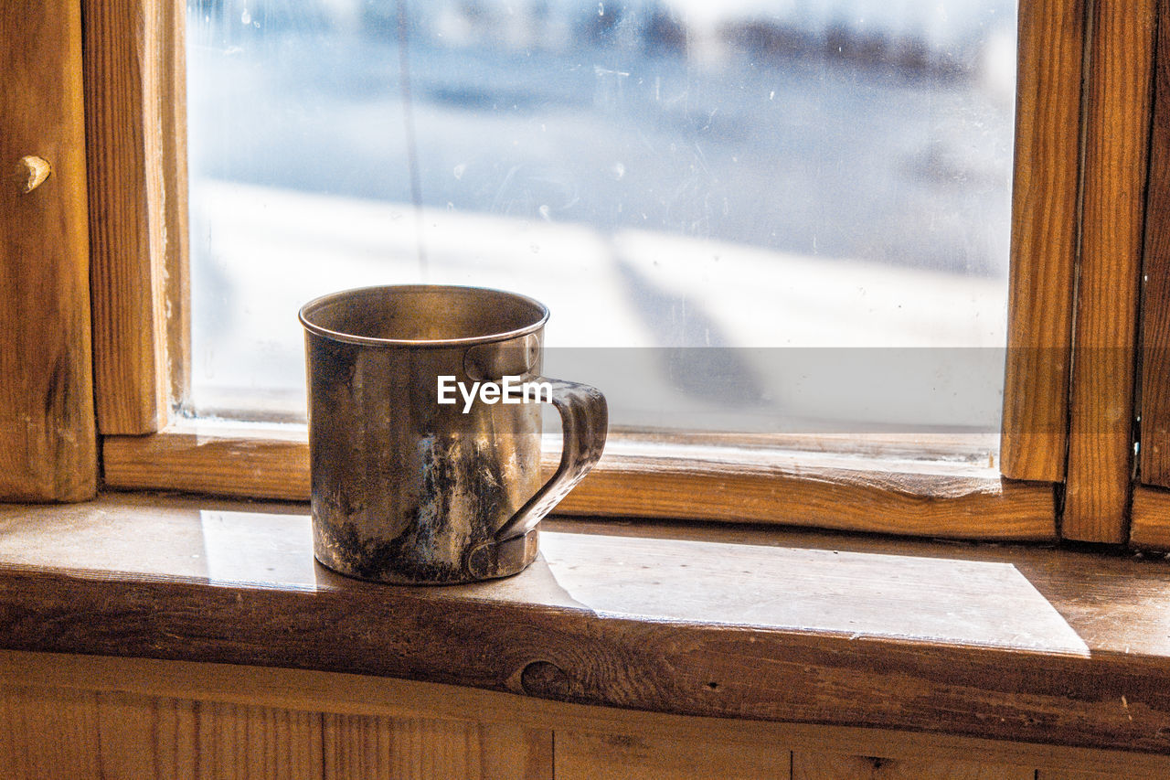 Old metal mug stands on a wooden window sill