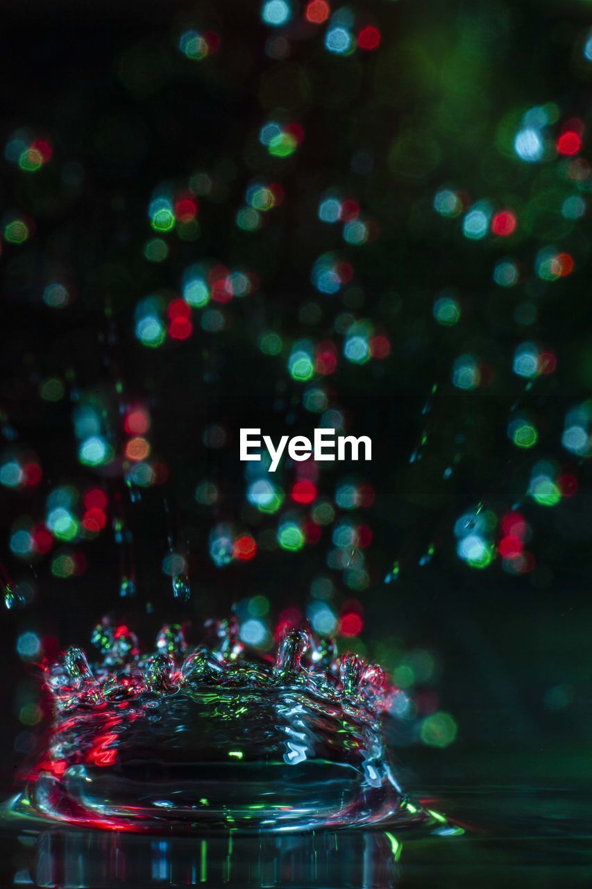 Close-up of splashing droplet against illuminated christmas lights