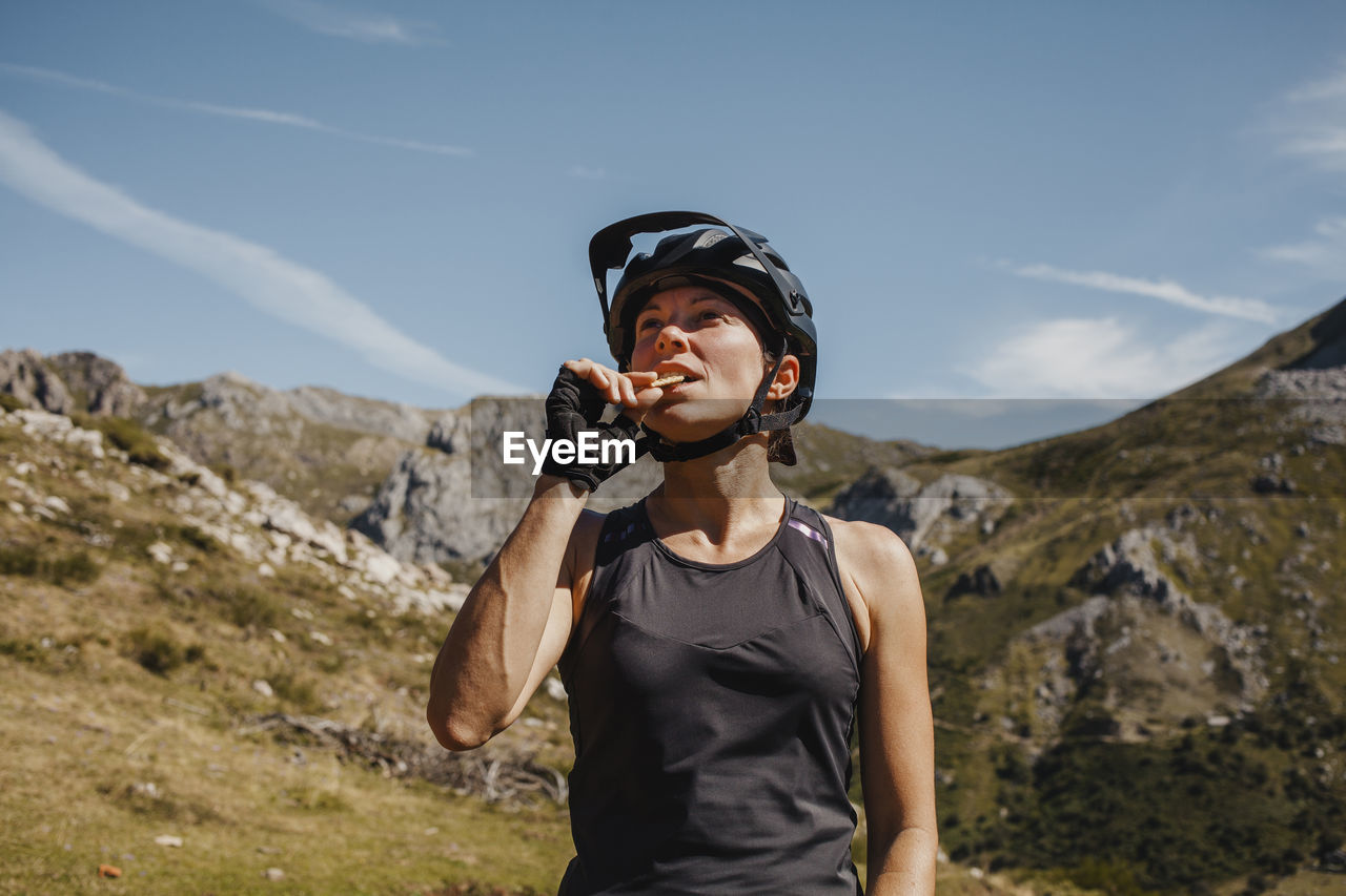 Woman wearing cycling helmet eating biscuit while standing against mountain at somiedo natural park, spain