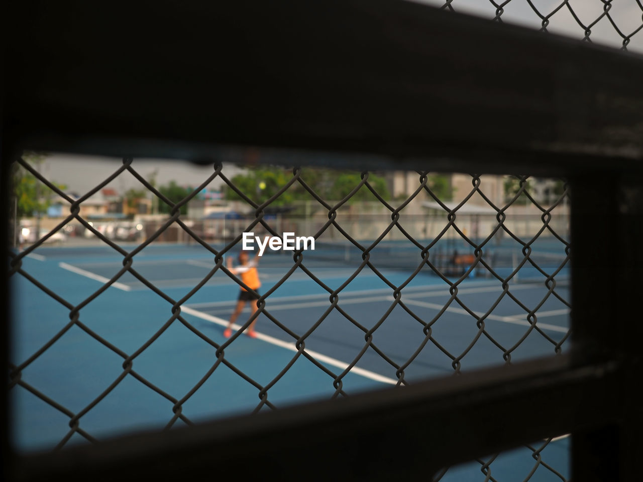 Blurred image of young asian tennis player serving a tennis ball with metal wire fence.